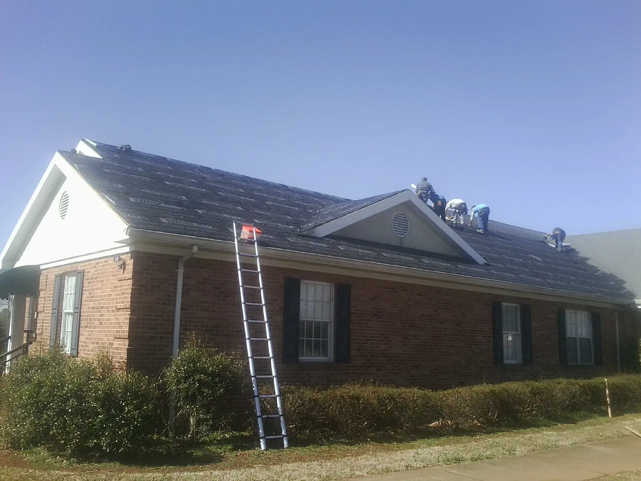 Crew tearing shingles off a brick ranch roof with a ladder set — Metal Roof Repair work by our crew in Wawaka