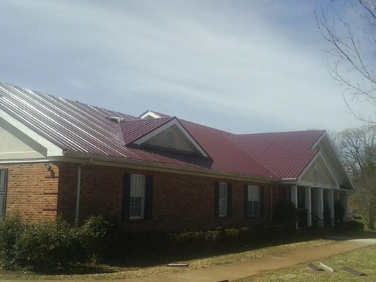 Red metal roof with gabled entries on a long brick building, from a Hail Damage Roof Repair job in Wawaka