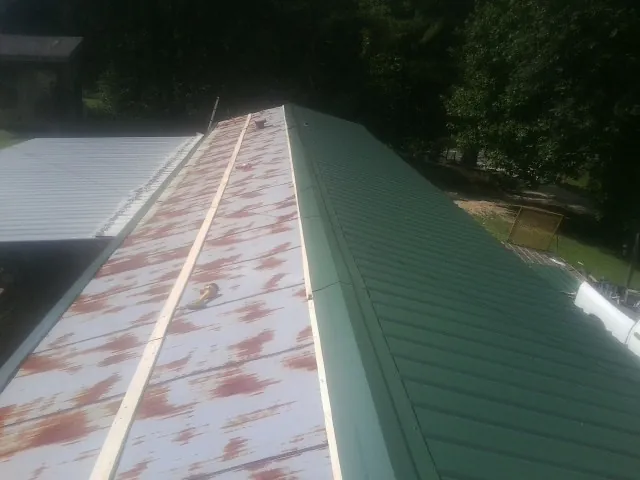 Old rusted panels beside newly installed green metal roofing — Wind Damage Roof Repair by Roofing Brothers in Wawaka
