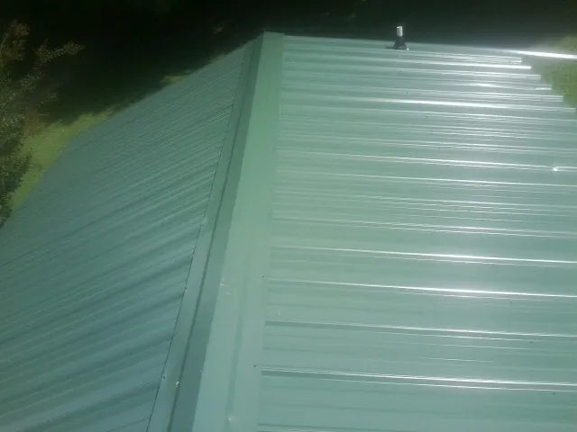 New green metal panels meeting at the ridge of a roof — Flat Roof Repair work by our crew in Wawaka