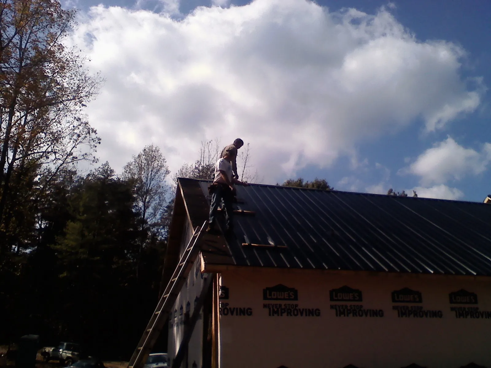 Roofer fastening dark metal panels high against a cloudy sky, from a Roof Inspection job in Wawaka