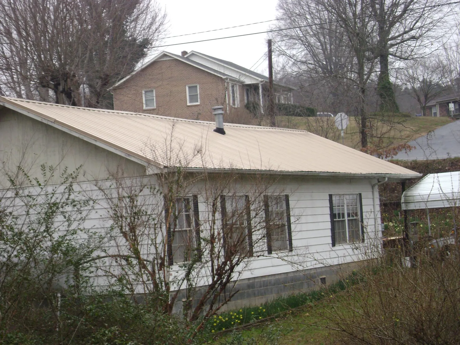 Tan metal roof on a white sided house set into a hillside — Commercial Roofing by Roofing Brothers in Wawaka