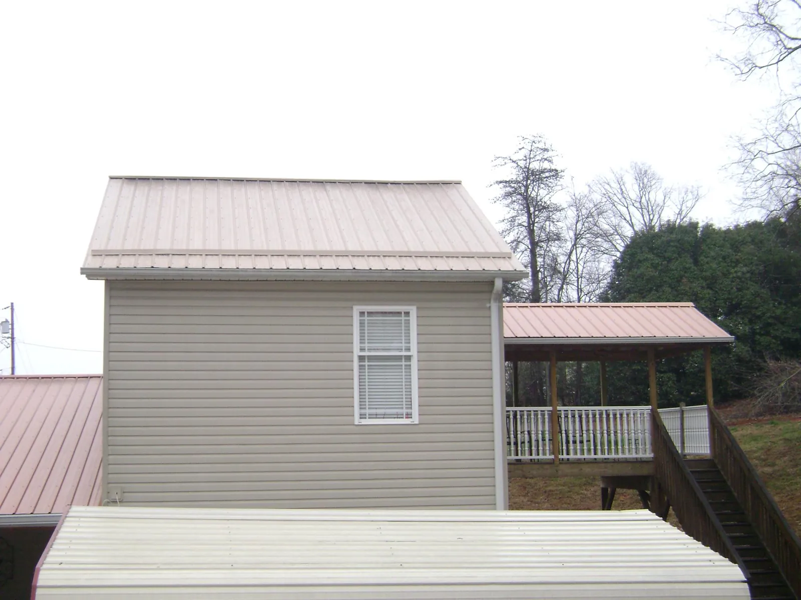 Tan metal roofs on a two story addition and attached porch, from a Roof Replacement job in Wawaka
